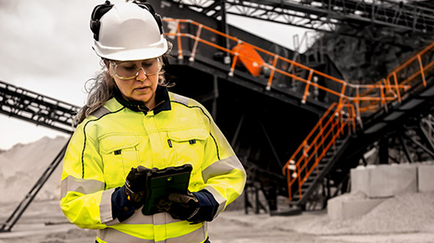 A woman in work clothes and helmet standing in front of a screening station at a quarry