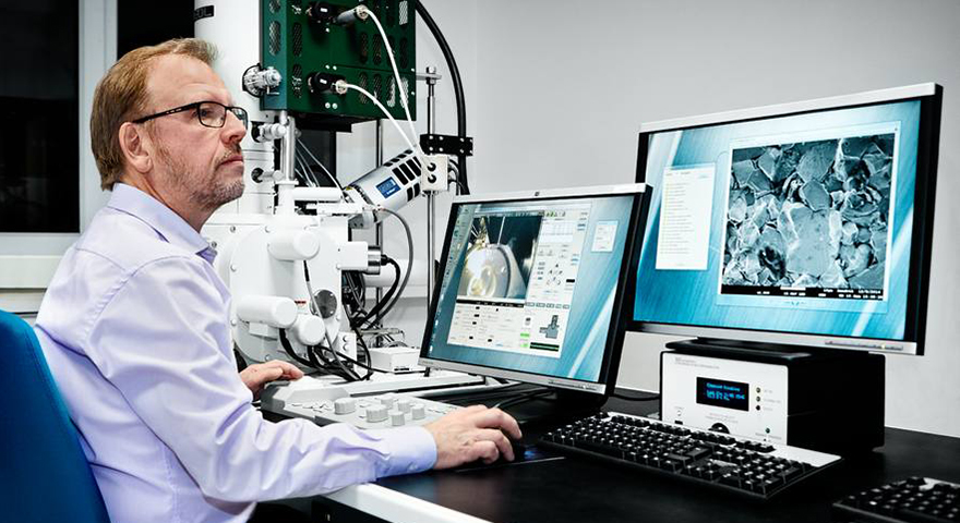 A man at a desk with a microscope and two monitors