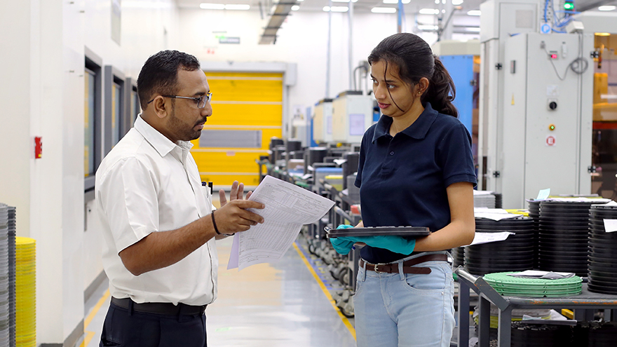 A man and a woman standing in a production environment next to a trolley with trays with inserts