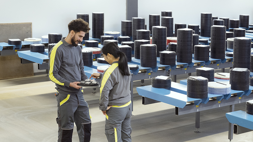 A man and a woman standing in a production environment next to several tables with trays with inserts