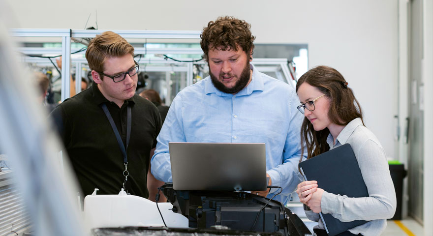 Three persons standing looking at the same laptop