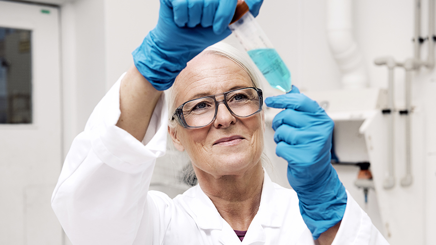 A woman wearing blue plastic gloves holding a test tube