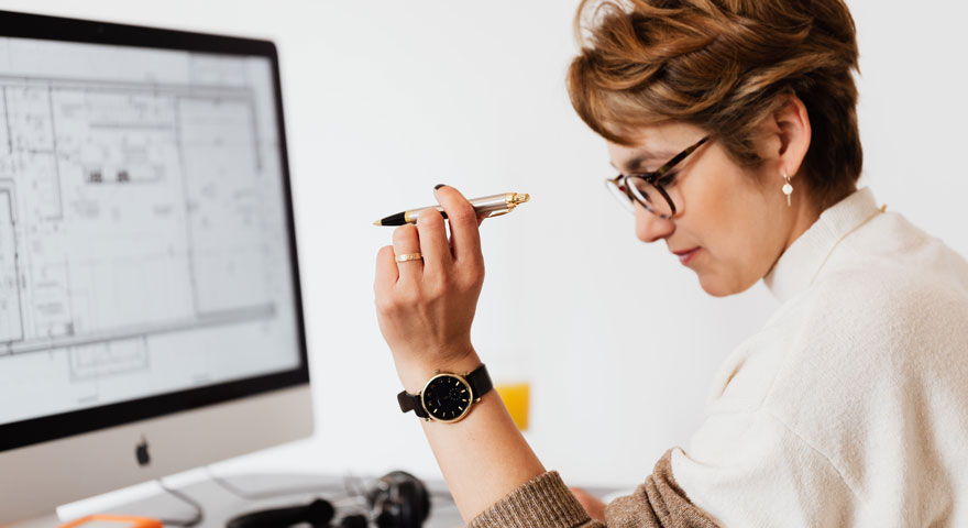 A woman sitting at a desk with a computer screen displaying a schematic drawing